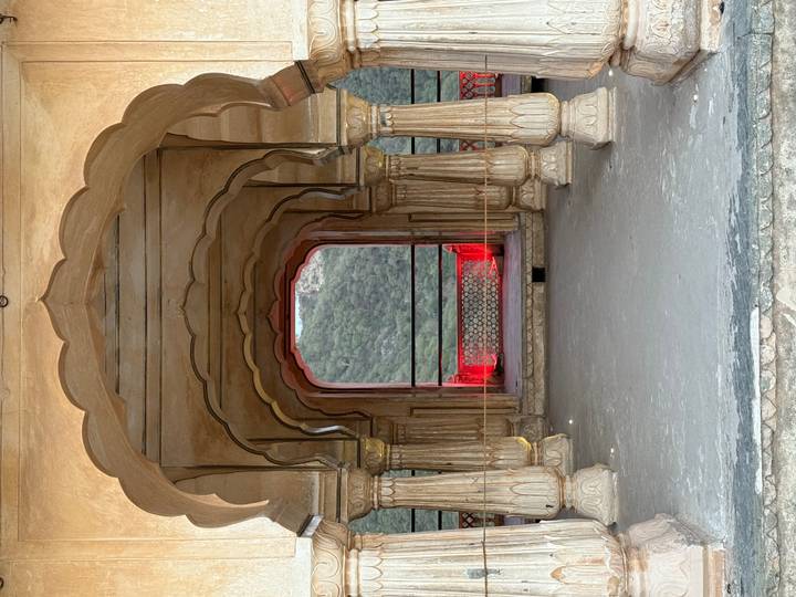 Symmetrical stone archway framing forested hills, accented by dramatic red lights.