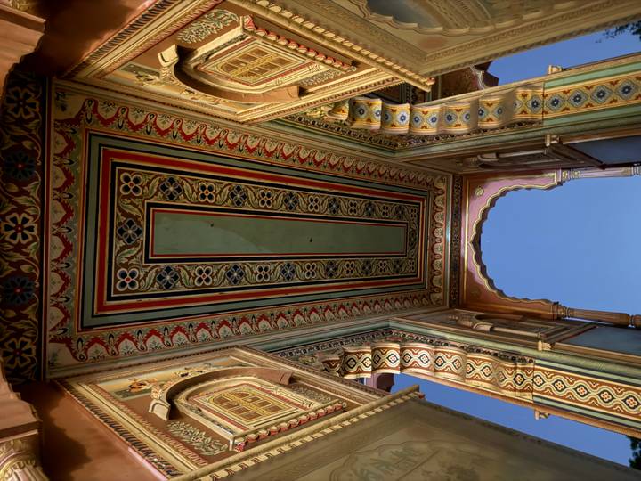 Upward view of a richly painted ceiling with intricate geometric and floral designs inside an Indian palace arch.