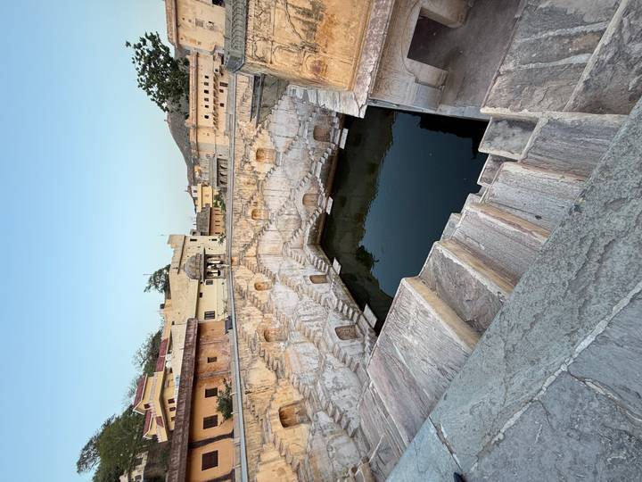 Stone stepwell filled with dark green water surrounded by weathered yellow walls and terraces.
