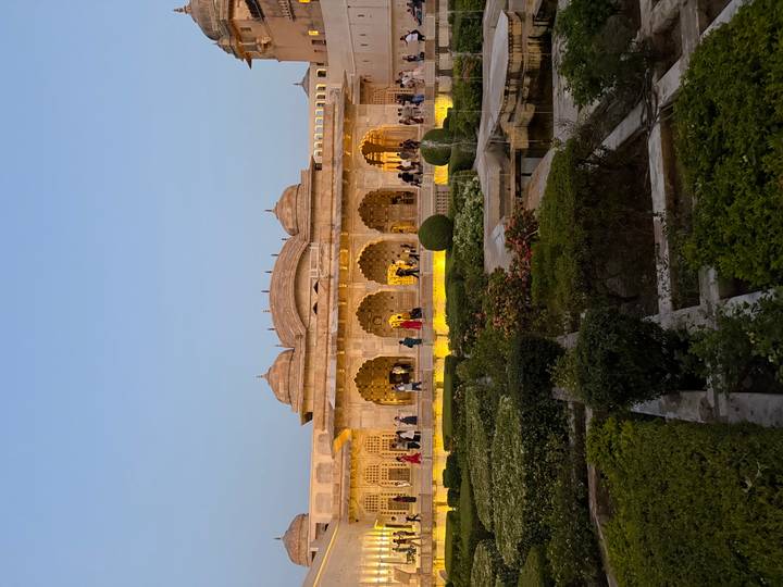 Illuminated Mughal garden courtyard at dusk with visitors strolling past elegant sandstone arches.
