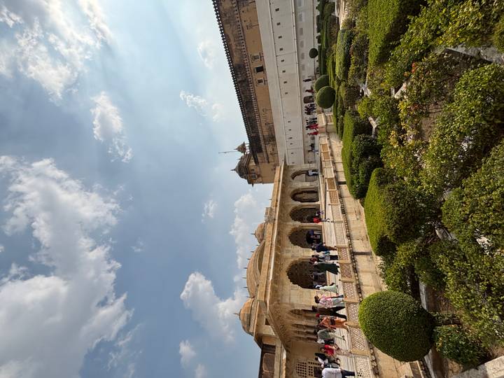 Visitors wander through the ornate sandstone arches and manicured garden courtyards of Amber Fort under a bright sky.