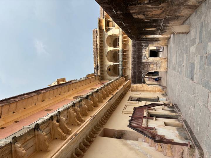 Stone corridors, balconies, and arches of an inner courtyard at Amber Fort with a lone visitor in the distance.