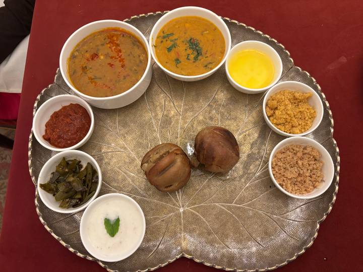 Traditional Rajasthani thali featuring dal, chutneys, ghee, bati breads, and sweet accompaniments arranged on a decorative platter.
