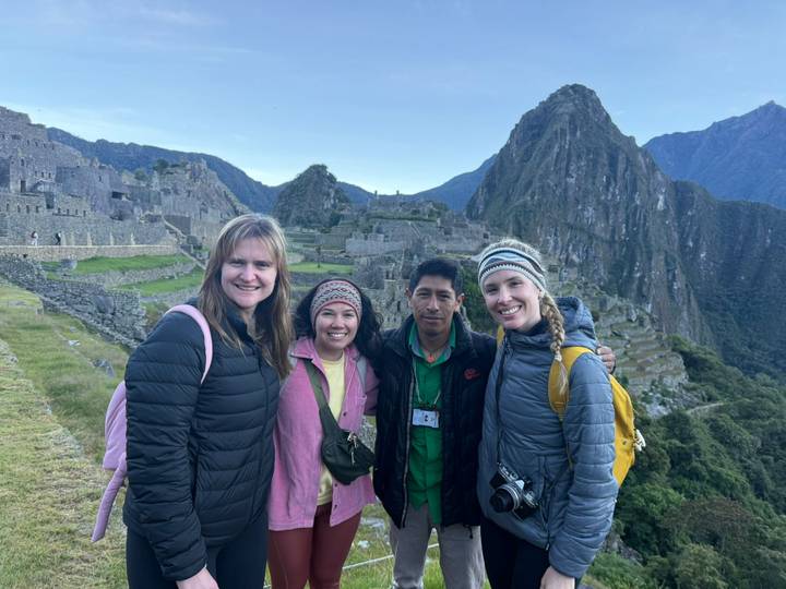 Group of hikers posing with Machu Picchu’s terraces and Huayna Picchu peak towering behind.