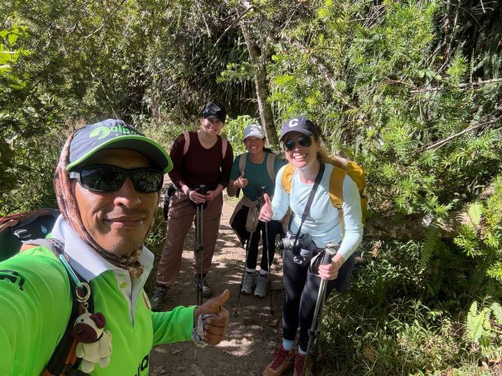 Trekking guide and hikers with poles smile on a lush forest trail.