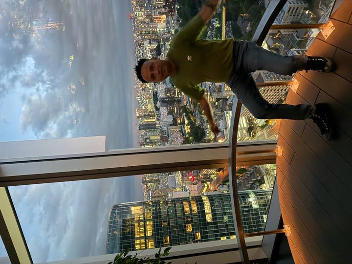 Man poses inside a high-rise observation deck overlooking Tokyo city lights at dusk
