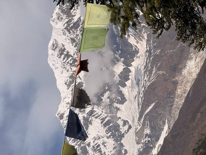 Prayer flags flutter in the foreground framing a dramatic ice-covered Himalayan face.