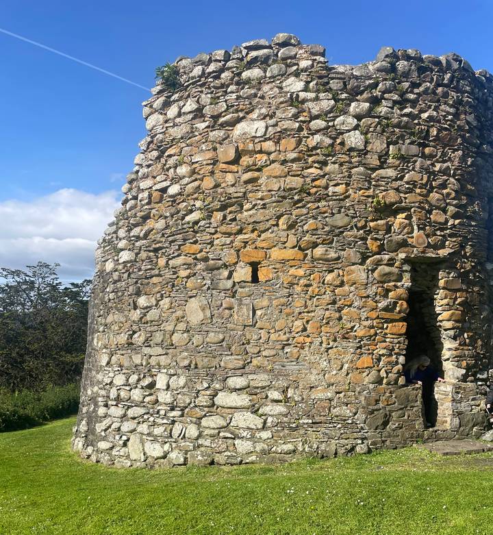 Close-up of a weathered stone round tower with a small doorway set against blue sky.