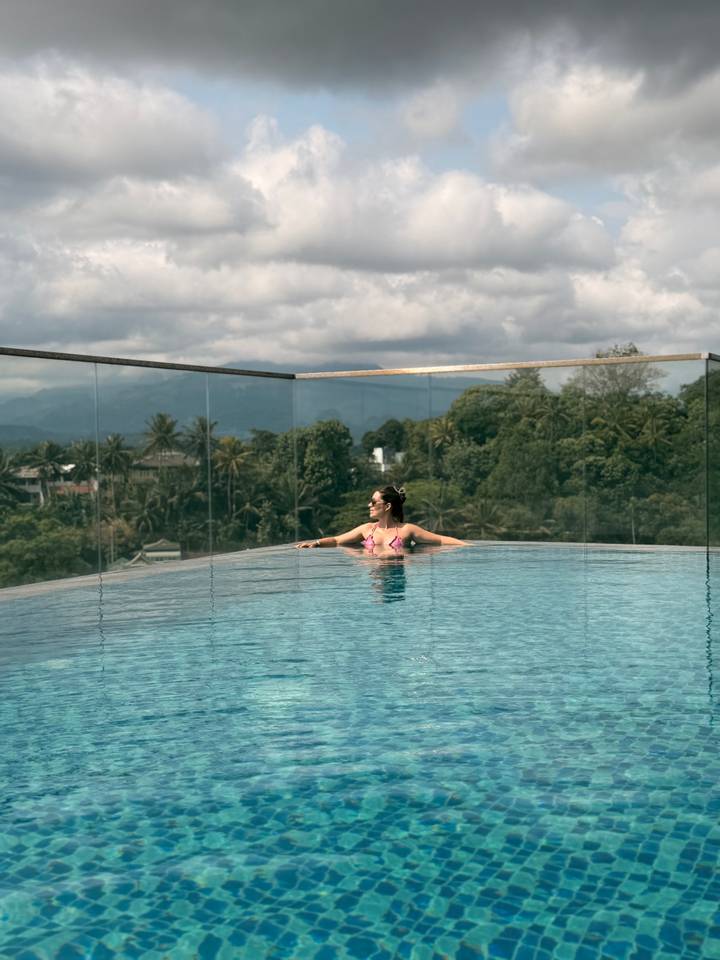 Woman relaxes in an infinity pool with jungle hills and mountains in the distance.