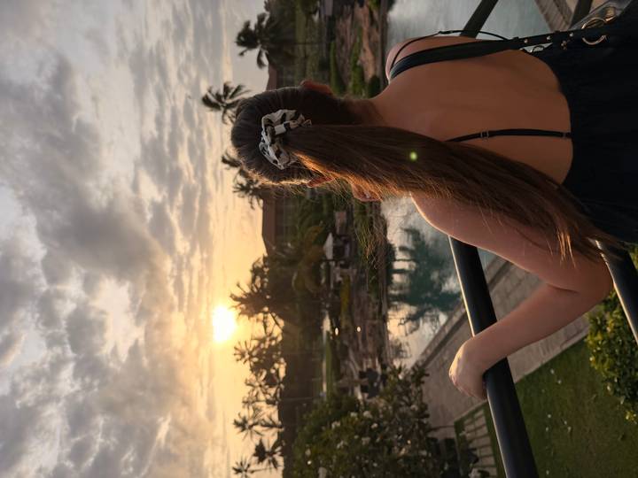 Back view of woman watching tropical sunset over resort pool and palms.