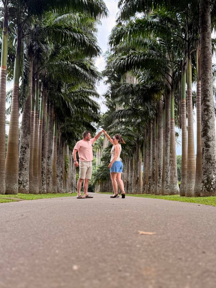 Couple dances in a grand avenue of tall royal palms in a botanical garden.