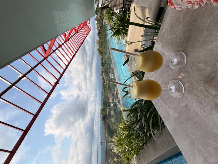 Two frosty fruit drinks on a marble table overlooking an elevated infinity pool and valleys.