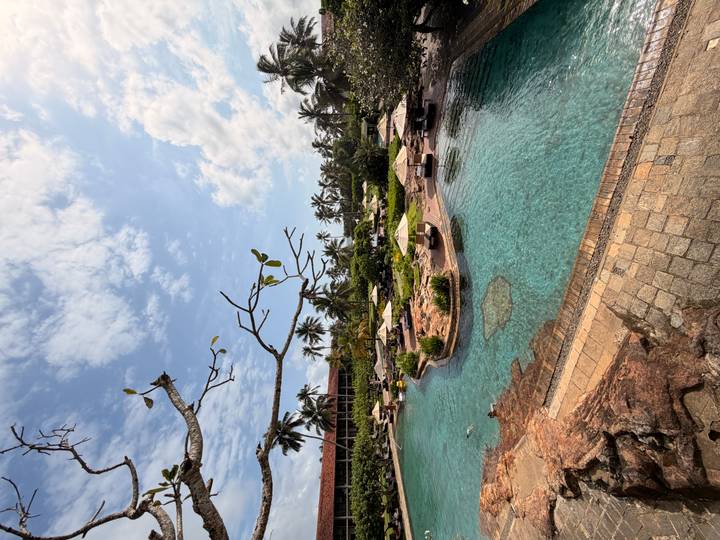Aerial view of expansive lagoon-style resort pool surrounded by palms under a bright sky.