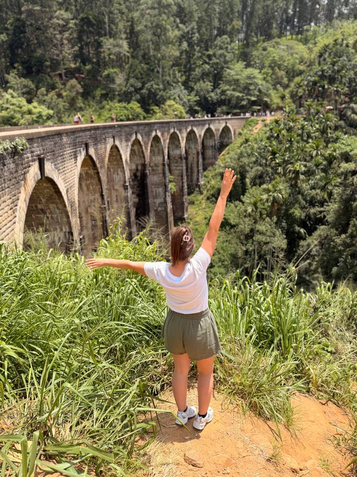 Traveller stretches arms toward the famous Nine-Arch Bridge amid lush jungle.