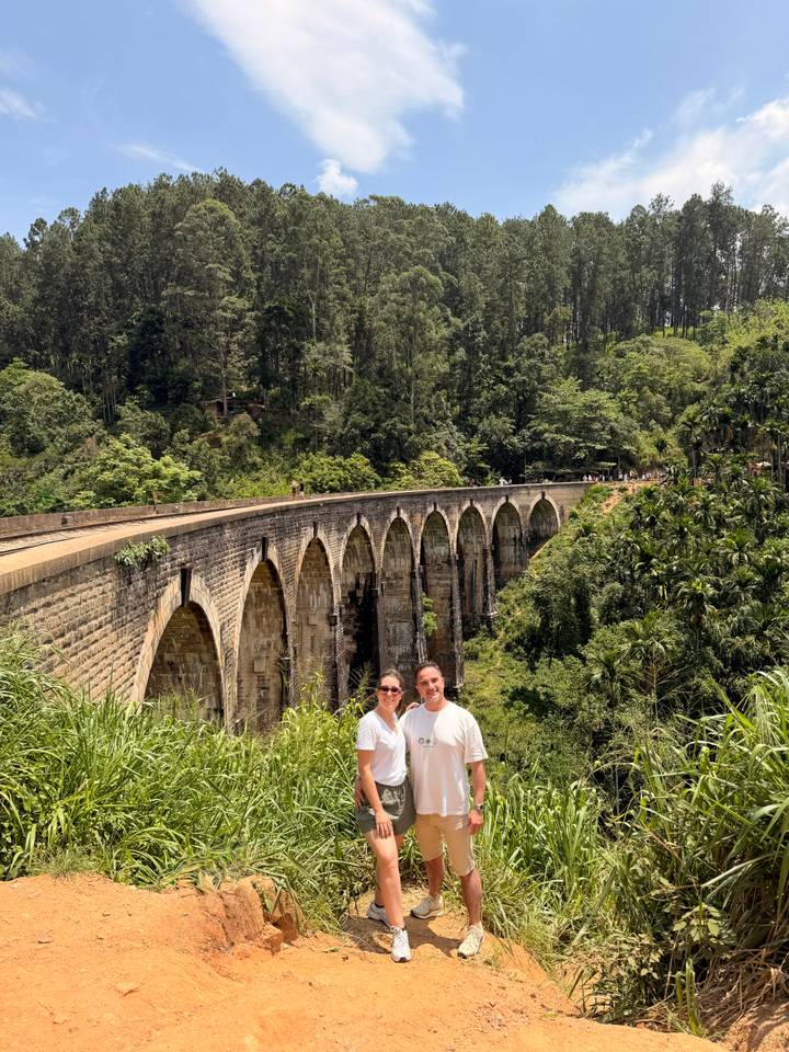 Couple stands beside the length of the iconic Nine-Arch Bridge stretching through jungle.