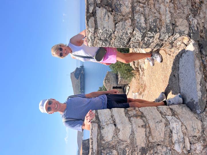 Senior couple stands between stone ruins overlooking the blue Adriatic coastline.