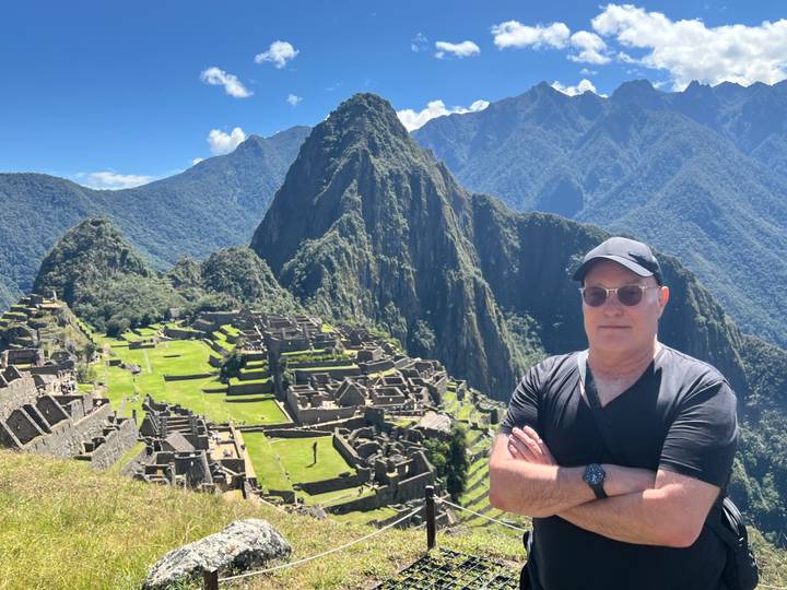 Traveler posing with arms crossed overlooking the ancient terraced ruins of Machu Picchu under blue skies