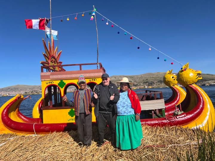 Tourist posing with two local islanders in front of a bright reed boat on Lake Titicaca