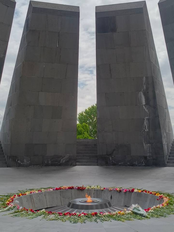 Two massive basalt pillars with a narrow gap framing green trees and cloudy sky, part of a solemn memorial complex.