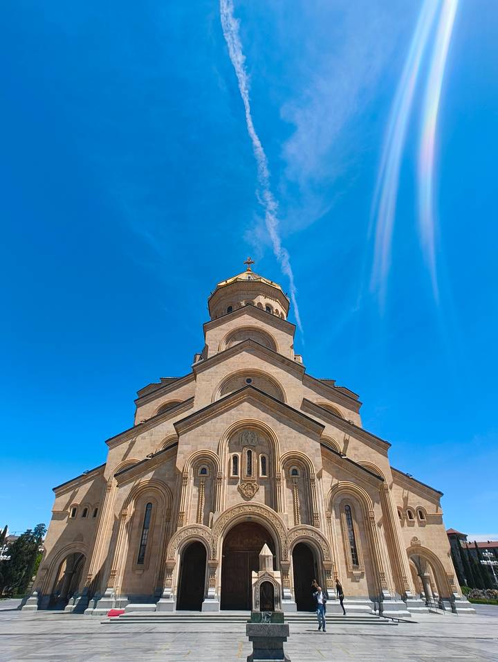 Low-angle shot of the Holy Trinity Cathedral’s golden dome and arched stone tiers contrasted against a vivid blue sky.