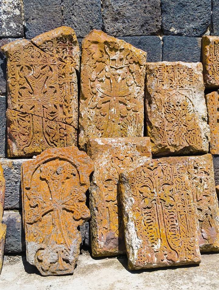 Close-up of intricately carved rusty-orange Armenian khachkar stone crosses stacked together.