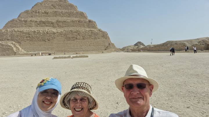 Three travellers take a selfie with the vast Saqqara pyramid complex sprawling behind them.