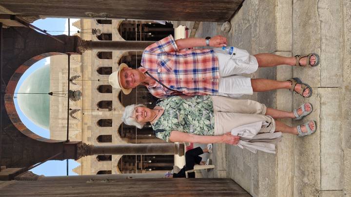Travellers standing inside an ancient mosque courtyard framed by tall arches and a green dome.