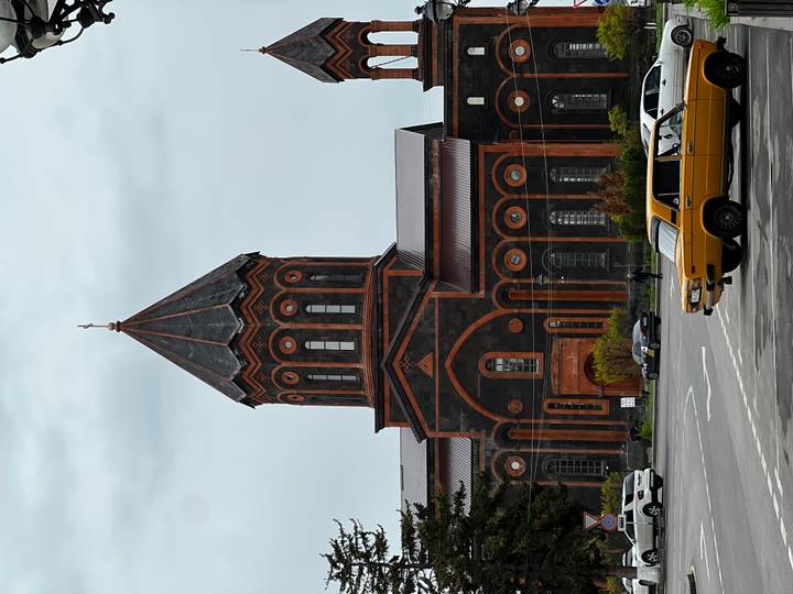 Distinctive black and red tuff stone church with tall conical spire; classic Soviet-era cars parked in front.