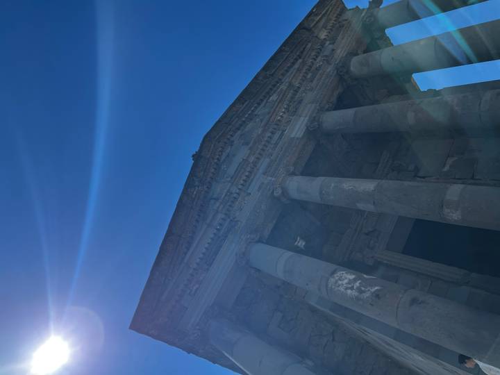 Low-angle shot of ancient Greco-Roman temple columns basking in strong sunlight with lens flare and bright blue sky.
