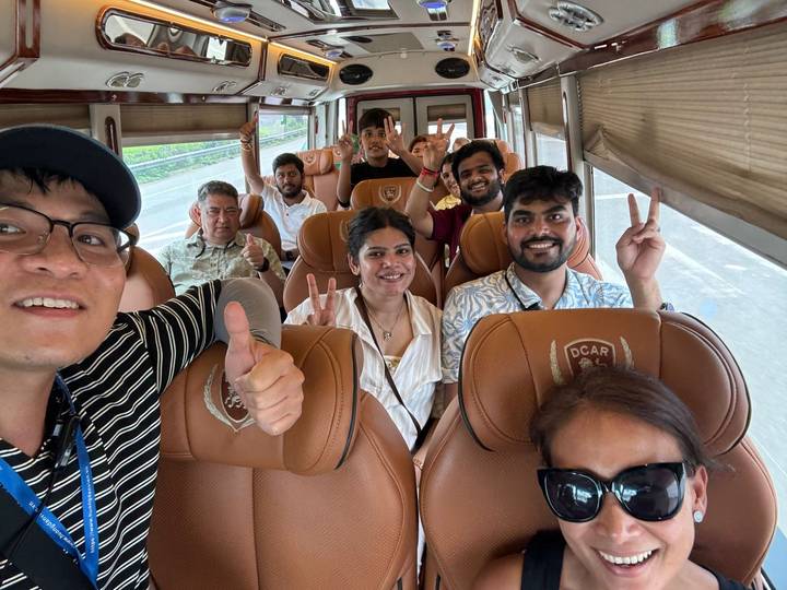Cheerful tour group giving thumbs up and peace signs inside a minibus.