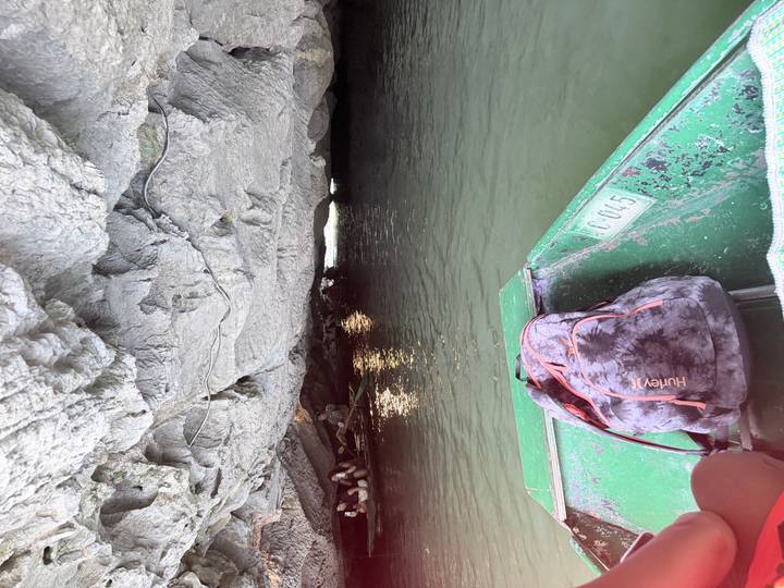 Small green boat entering a low limestone cave over dark water.