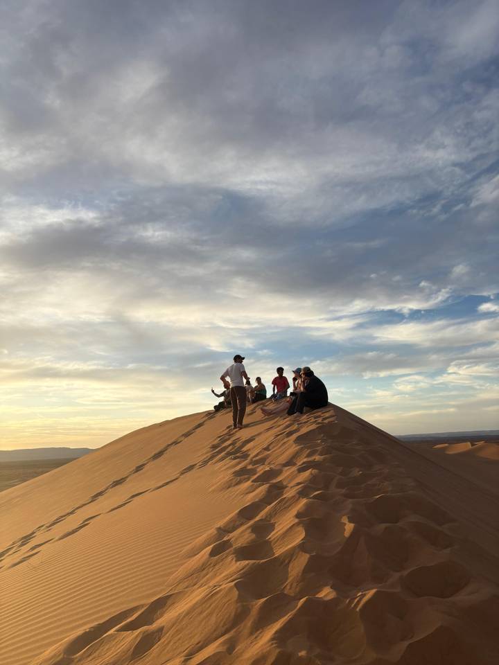 Travellers resting atop a dune under dramatic evening clouds.