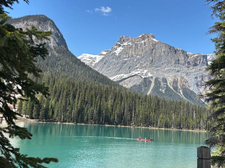 Vivid emerald lake with a red canoe gliding beneath soaring conifer-clad mountains.