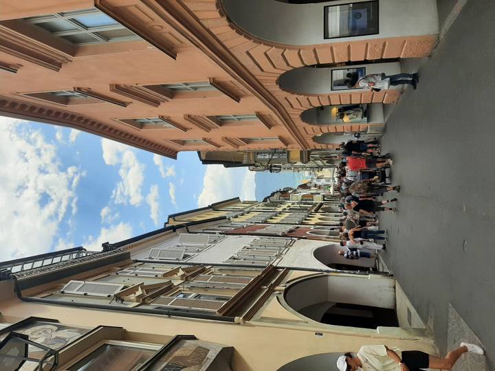 Bustling narrow street lined with pastel buildings and arches in Merano’s old town.