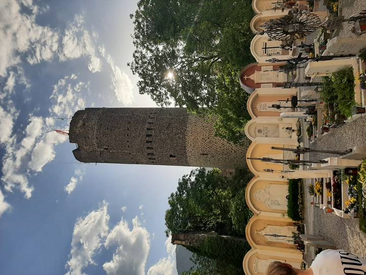 Stone medieval tower rises above a small cemetery against a bright afternoon sky.