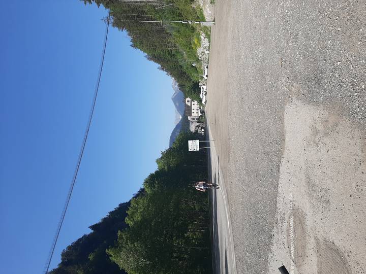 Cyclist rides across an open mountain parking area beneath a clear alpine sky.