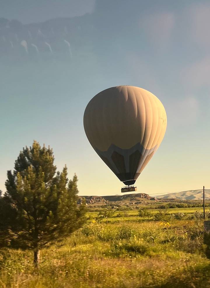 Golden sunrise light bathes a giant hot-air balloon drifting over Cappadocia valleys.