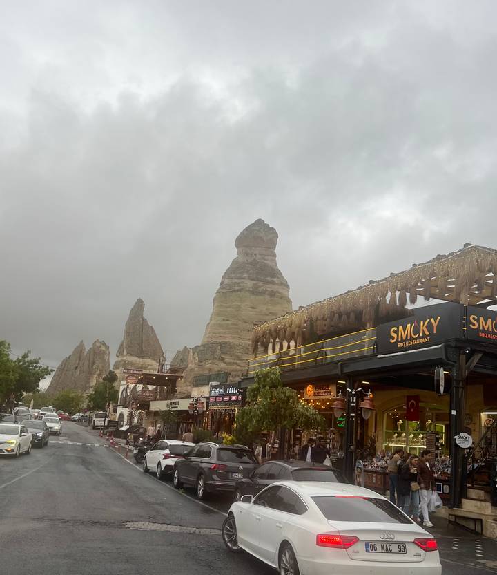 Iconic fairy-chimney rock rises beside lively cafés and shops beneath grey skies in Göreme.