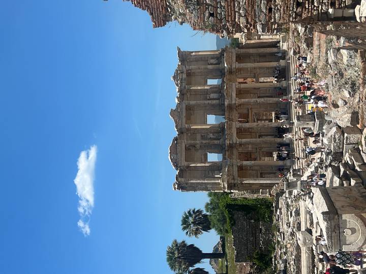 Majestic façade of the Library of Celsus towers over visitors amid sun-lit ancient ruins.