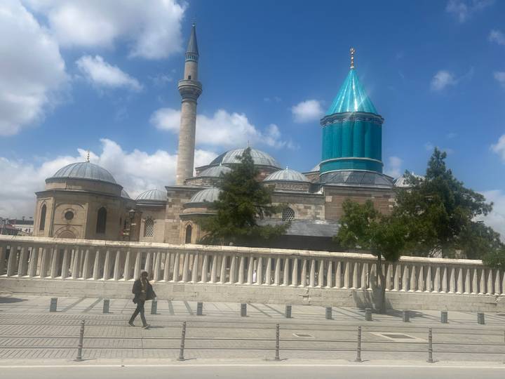 The turquoise-tiled dome and minaret of the Mevlana Museum gleam against a bright sky.