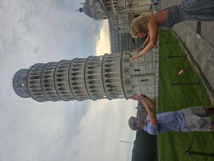 Two travelers pose playfully 'holding up' the iconic Leaning Tower of Pisa.