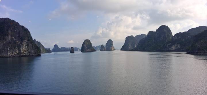 Towering limestone karsts rise from the calm waters of Ha Long Bay under a partly cloudy sky.