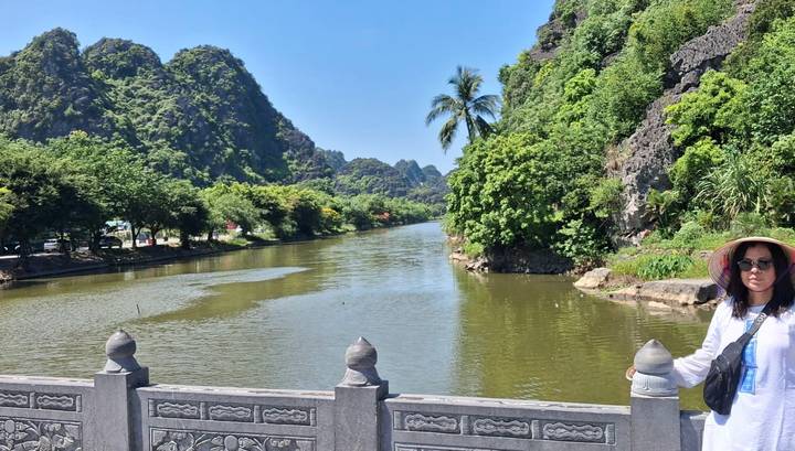 A lush river valley bordered by limestone cliffs and tropical trees, with a lone tourist posing at the balustrade.
