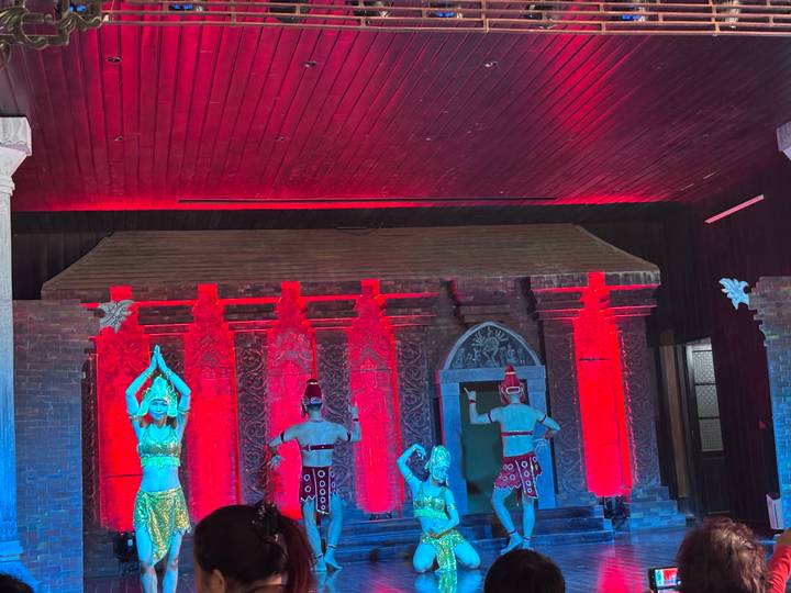 Traditional dancers in ornate costumes perform on a stage lit with dramatic red and blue lighting.