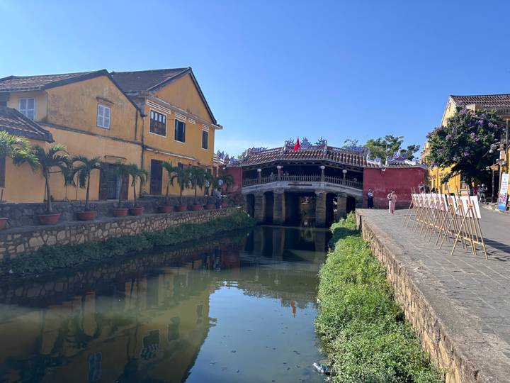 Hoi An’s iconic Japanese Covered Bridge spans a quiet canal amid yellow heritage buildings and clear reflections.
