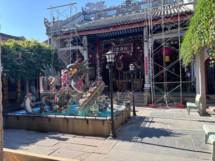 An ornate dragon mosaic fountain stands in a courtyard of a historic Chinese-Vietnamese temple under restoration.