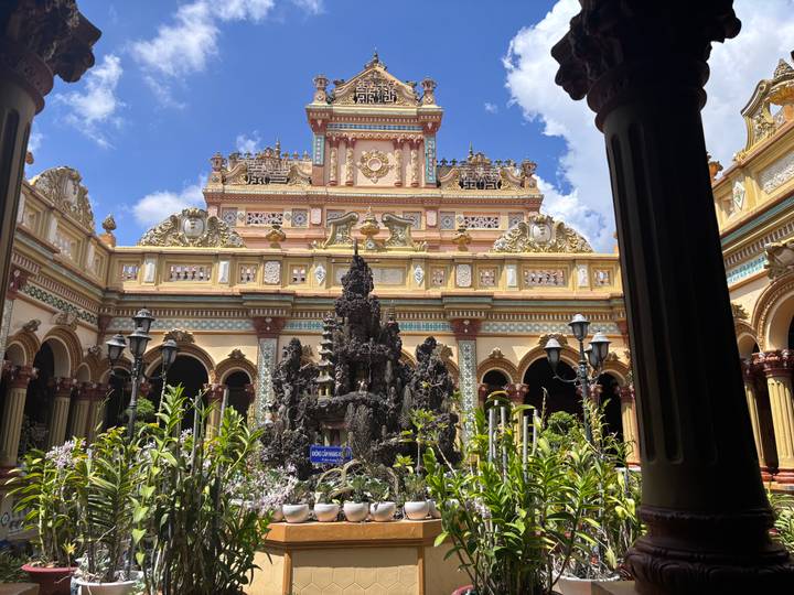 Ornate pastel-coloured façade and courtyard garden of a Vietnamese temple richly decorated with carvings.