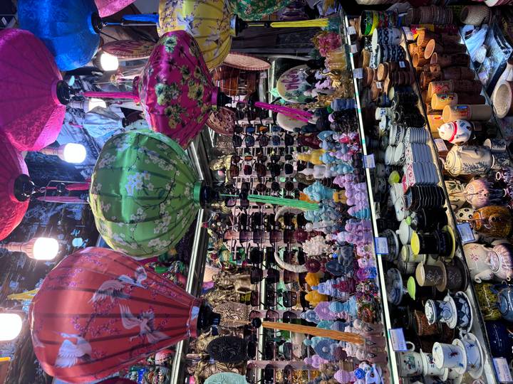 A vibrant market stall packed with colourful silk lanterns, ceramics and souvenirs under warm lighting.