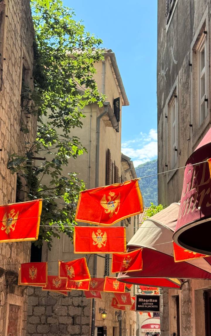 Red Montenegrin flags with the golden double-headed eagle hang across a narrow stone alleyway.