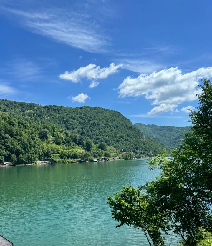 A serene green river winds between forested hills under a bright blue summer sky.